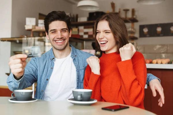 Happy young couple sitting at the cafe table and showing plastic credit card
