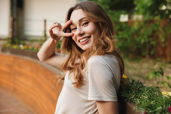 Sorridente Ragazza Abiti Casual Guardando Fotocamera Mostrando Gesto Pace Mentre — Foto Stock