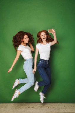 Tam uzunlukta atlama birlikte izole yeşil arka plan üzerinde iken bir selfie alarak iki neşeli genç Kızıl saçlı kız portresi