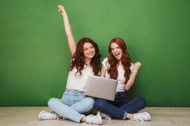 İki dizüstü bilgisayar ve üzerinde yeşil arka plan izole kutlama bir katta oturan genç Kızıl saçlı kız gülümseyerek portresi