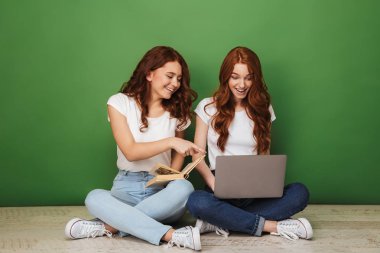 İki parmak üzerinde yeşil arka plan izole bir kitap ile bir yerde otururken dizüstü bilgisayarda işaret genç Kızıl saçlı kız gülümseyerek portresi