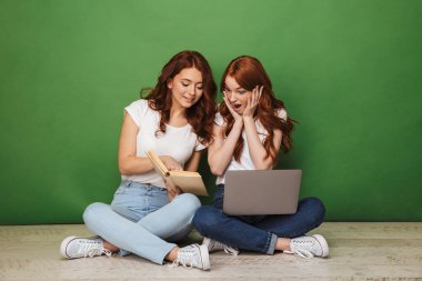 İki dizüstü bilgisayar ve kağıt kitap üzerinde yeşil arka plan izole bir katta oturan genç Kızıl saçlı kız gülümseyerek portresi