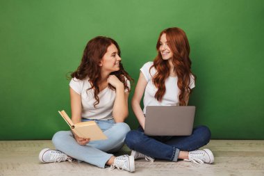 İki dizüstü bilgisayar ve kağıt kitap üzerinde yeşil arka plan izole bir katta oturan genç Kızıl saçlı kız gülümseyerek portresi