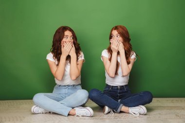 Yeşil arka plan üzerinde izole elleri olan bir taban ve kapağı dudaklarından oturan iki sürpriz genç Kızıl saçlı kız portresi