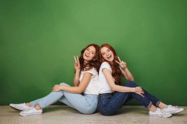 İki bir katta oturan ve üzerinde yeşil arka plan izole barış hareketi gösteren genç Kızıl saçlı kız gülümseyerek portresi