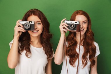 İki Kızıl saçlı kadınlar 20'li yaşlarda görüntü closeup holding ve retro kamera üzerinde izole photopraphing yeşil arka plan