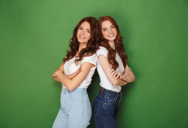 两个快乐的女孩20S 与生姜头发在不经意的穿着微笑着在相机和站回背部与双臂越过绿色背景隔离 — 图库照片