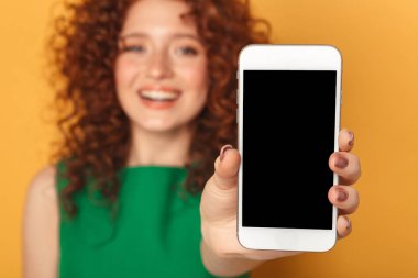 İçinde boş ekran cep telefonu izole sarı arka plan üzerinde gösterilen bir memnun Kızıl saçlı kadın portresi