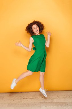 Tam uzunlukta atlama izole sarı arka plan üzerinde iken elbise poz içinde bir heyecan Kızıl saçlı kadın portresi