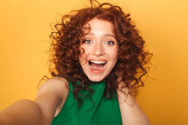 İçinde sarı arka plan üzerinde izole bir selfie alarak gülünecek bir kızıl saçlı kadın portresi kapatın