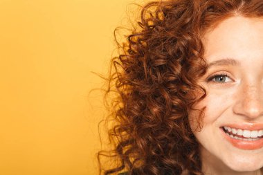 Yarım yüz yakın çekim üzerinde sarı arka plan izole kamera bakarak gülümseyen bir kıvırcık saçlı kadın portresi