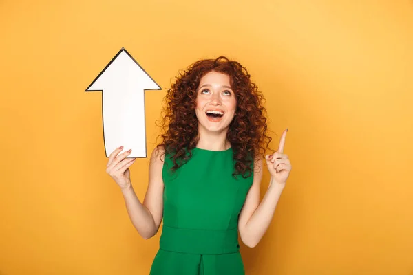 一个快乐的红头发的女人的肖像指向与黄色背景的箭头隔离 — 图库照片