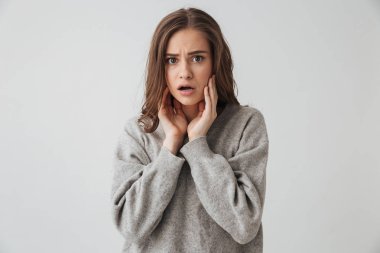 Yanaklarını dokunmak ve gri arka plan üzerinde kameraya bakarak kazaklı şok esmer kadın