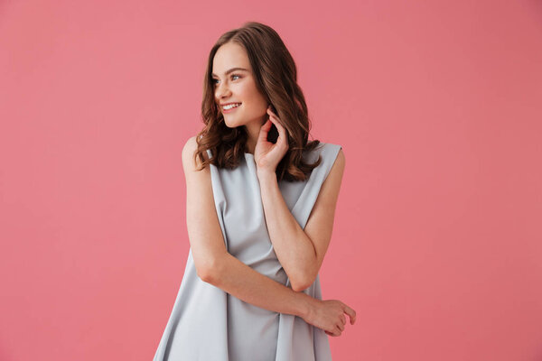 Image of pretty cheerful young woman standing isolated over pink background looking aside.