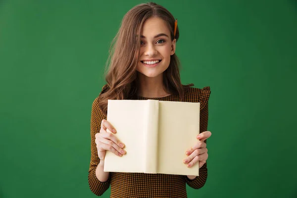 孤立した本を保持している緑の背景に立っている若い女性の画像 — ストック写真