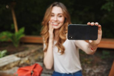Açık havada bankta otururken selfie alarak genç kız gülümseyerek
