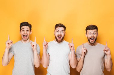 Üç genç mutlu adam sarı arka plan üzerinde izole kopya alanı işaret
