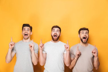 Üç genç erkekler üzerinde sarı arka plan izole kopya alanı işaret heyecanlı