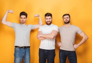 Üç genç kendine güvenen erkekler üzerinde sarı arka plan izole kamera arıyorum