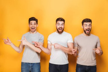 Üç genç neşeli adam uzakta sarı arka plan üzerinde izole kopya alanı işaret