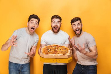 Üç genç neşeli adam izole sarı arka plan üzerinde büyük bir pizza holding