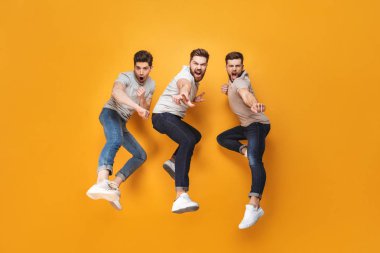 Üç genç sarı arka plan üzerinde neşeli erkekler birlikte atlama izole