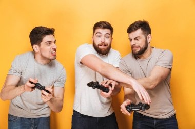 Üç genç komik adam video sarı arka plan üzerinde izole oyunları oynarken oyun çubukları holding