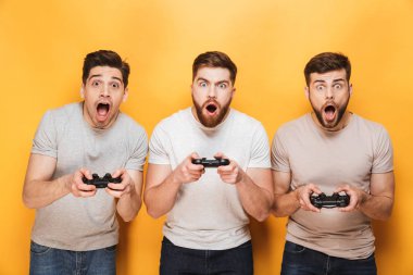 Üç genç şok adam sarı arka plan üzerinde izole video oyunları oynarken oyun çubukları holding