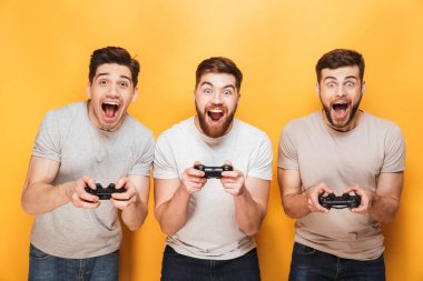 Üç genç mutlu adam sarı arka plan üzerinde izole video oyunları oynarken oyun çubukları holding