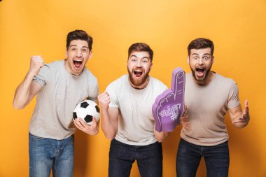 Üç genç neşeli erkekler futbol taraftarları sarı arka plan üzerinde izole kutlama