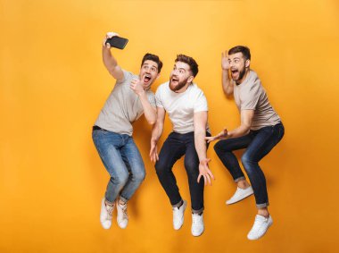 Üç genç mutlu erkek atlama izole sarı arka plan üzerinde iken bir selfie birlikte alarak