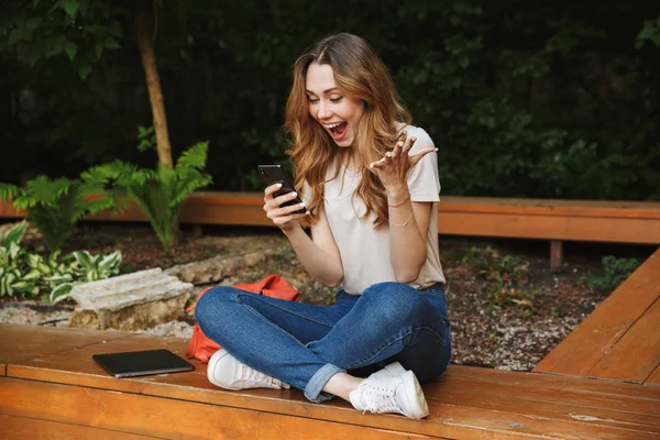 Bir tezgah açık havada üzerinde otururken cep telefonu kullanan genç kız heyecanlı