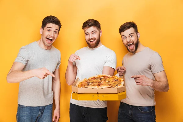 黄色背景に分離した大きなピザを保持している つの若い幸せな男性 — ストック写真