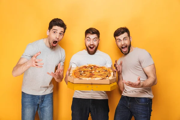 黄色背景に分離した大きなピザを保持している 人のうれしそうな男性 — ストック写真