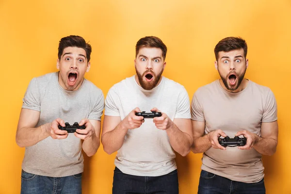 Tres Jóvenes Sorprendidos Hombres Sosteniendo Joysticks Mientras Jugaban Videojuegos Aislados —  Fotos de Stock