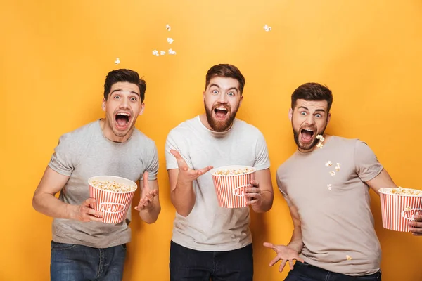 Three Young Excited Men Eating Popcorn Celebrating Isolated Yellow Background — Stock Photo, Image