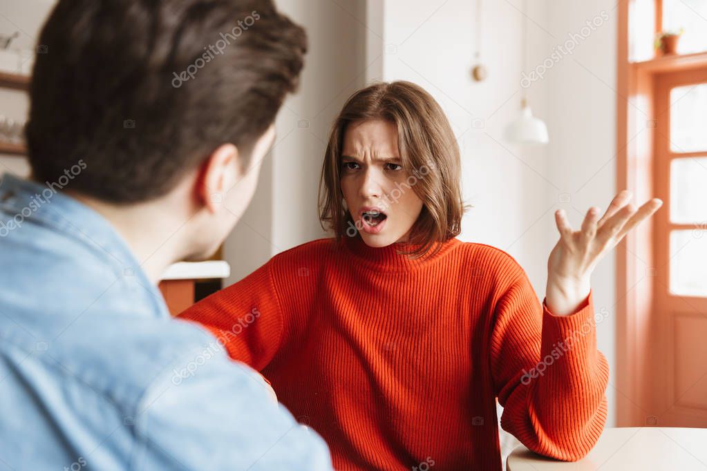 Angry young woman having an argument with her boyfriend at a cafe indoors