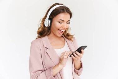 Görüntü Genç Sevimli güzel kadının beyaz duvar arka plan müzik dinleme üzerinde cep telefonu kullanarak kulaklık ile izole.