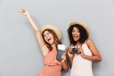 Pasaport ve bilet tutarak ve gri arka plan üzerinde kutluyor yaz elbise giymiş iki neşeli genç kadın portresi