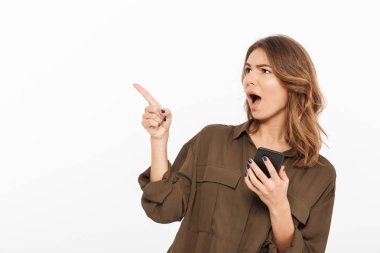 Cep telefonu tutan ve beyaz arka plan üzerinde uzak izole parmak işaret neşeli bir genç kadın portresi
