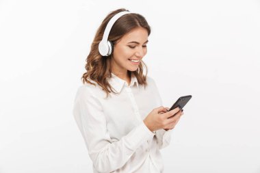 Beyaz arka plan üzerinde izole cep telefonu kullanırken kulaklık ile müzik dinlemek bir gülümseyen genç iş kadını portresi