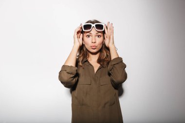 Süre ayakta ve beyaz arka plan üzerinde izole kamera bakarak poz güneş gözlüklü genç ve güzel bir kadın portresi