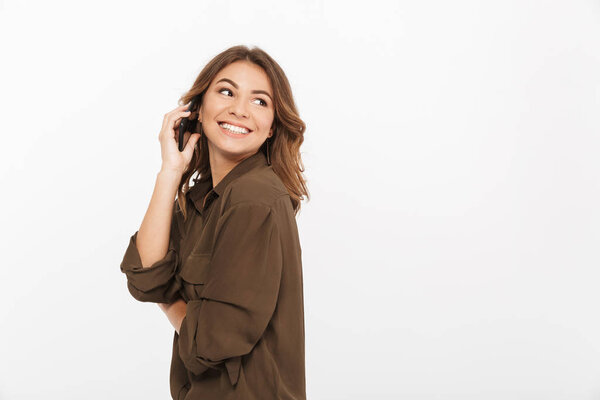 Портрет улыбающейся молодой женщины, разговаривающей по мобильному телефону и смотрящей в сторону на белом фоне
