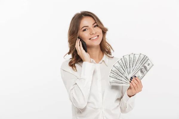 一个兴奋的年轻的商业妇女的肖像持有钞票和谈论在白色背景下的手机隔离 — 图库照片
