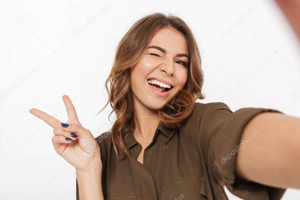 Portrait of a smiling young woman taking selfie with mobile phone isolated over white background