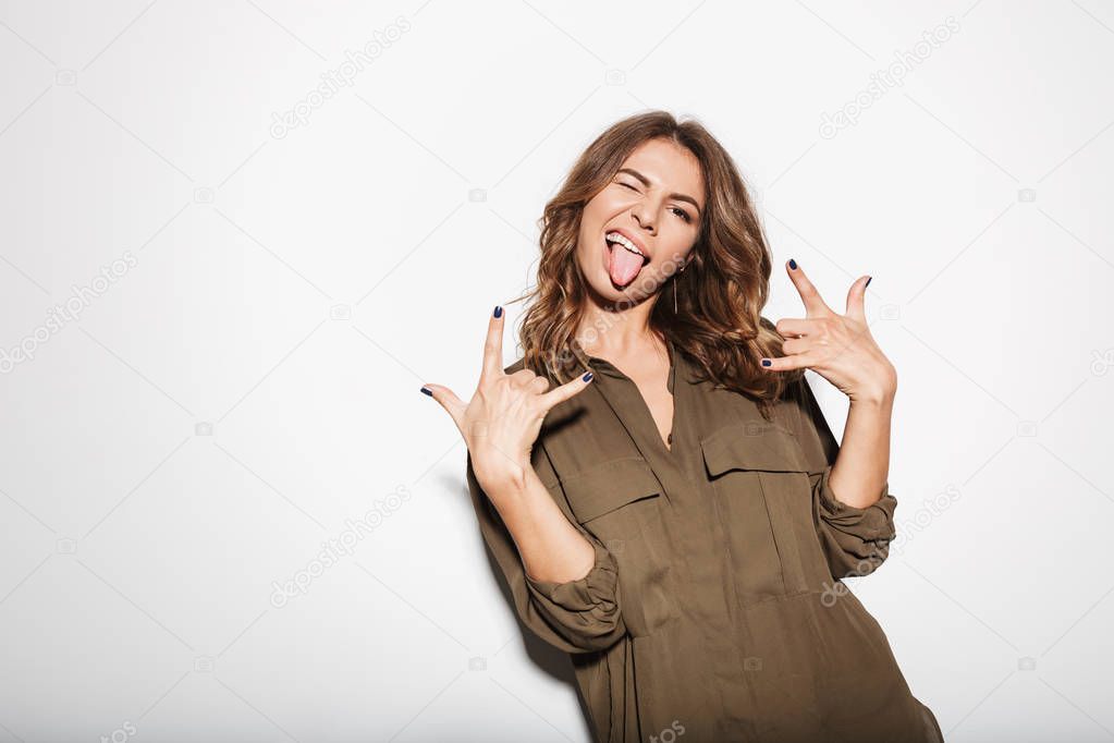 Portrait of a happy young woman having fun and showing horns up gesture isolated over white background