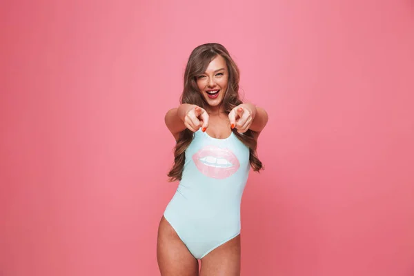 一个兴奋的年轻女子的肖像 身着泳装指着在粉红色背景下的相机孤立的手指 — 图库照片