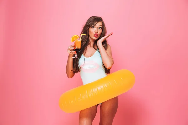 一个可爱的年轻女子的肖像 穿着泳装摆着充气戒指 并举行了粉红色背景的鸡尾酒隔离 — 图库照片
