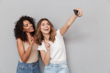 İki mutlu genç kadın ile cep telefonu gri arka plan üzerinde izole selfie alarak portresi