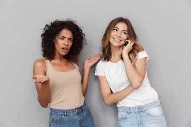 Birlikte iki genç ve güzel kadının portresi, gülümseyen kadın cep telefonu üzerinde konuşurken gri arka plan üzerinde izole